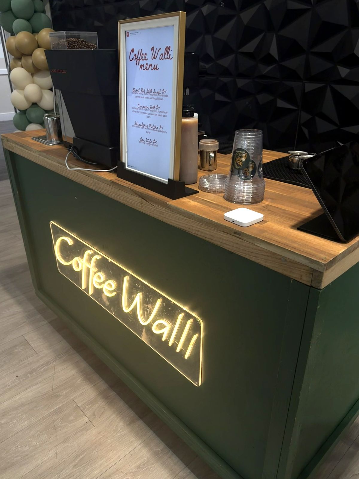 Coffee Walli stand set up with a framed menu, cups, and a balloon garland