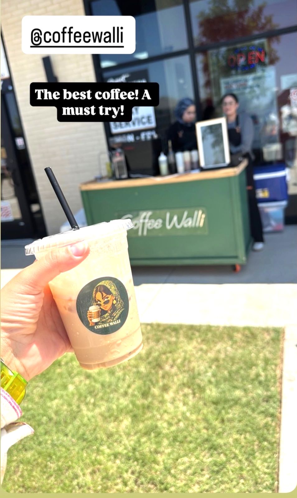 A customer holding an iced latte in front of the outdoor Coffee Walli stand